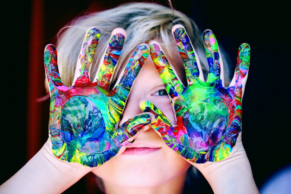 Child with rainbow marbled paint on hands in front of face